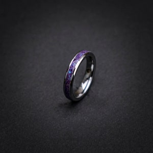 Op de afbeelding: Een zilveren ring van wolframcarbide met een paarse inlay. De inlay heeft een gevlekt patroon.