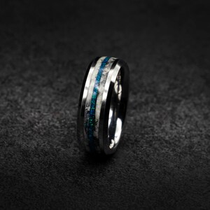 May include: A silver ring with a black band and two thin blue and white stripes.