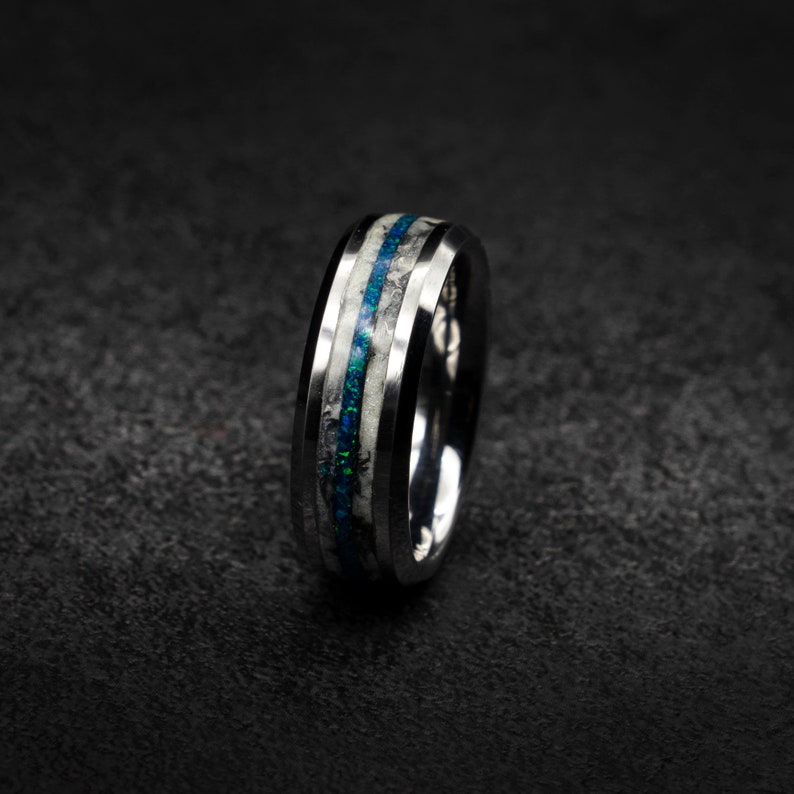 May include: A silver ring with a black band and two thin blue and white stripes.