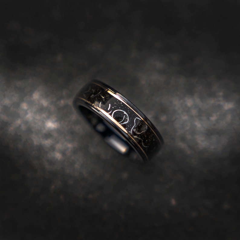 May include: A black and gold ring with a unique design. The ring has a thin gold band and a black band with a pattern of white dots.