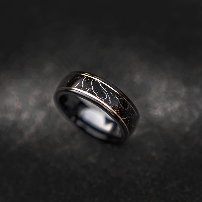 May include: A black tungsten carbide ring with a gold inlay featuring a swirling pattern.
