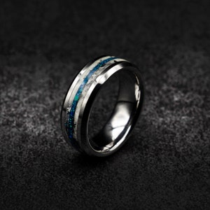 May include: A silver tungsten carbide ring with a blue and white inlay. The ring has a bevelled edge and a polished finish.