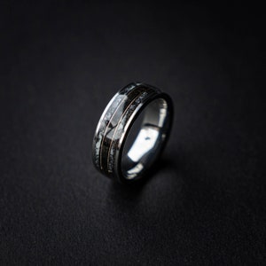 Puede incluir: Un anillo de plata con una incrustación negra y blanca. La incrustación tiene un patrón moteado.