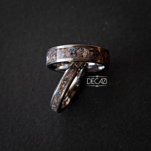 May include: Two silver rings with a brown and blue inlay. The rings are stacked on top of each other. The rings are on a dark gray background. The text "DECAZI" is visible in the background.