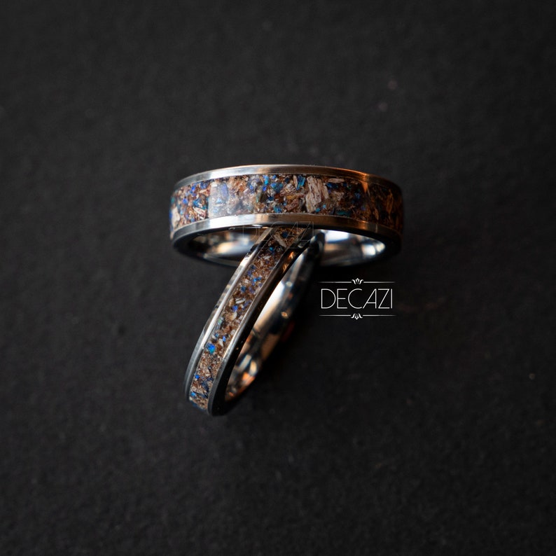 May include: Two silver rings with a brown and blue inlay. The rings are stacked on top of each other. The rings are on a dark gray background. The text "DECAZI" is visible in the background.