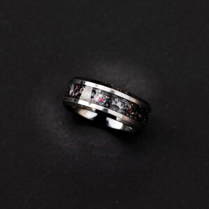 May include: A silver ring with a black and white inlay. The inlay has a speckled pattern with hints of red.