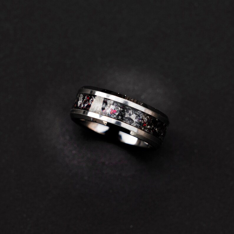 May include: A silver ring with a black and white inlay. The inlay has a speckled pattern with hints of red.
