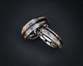 May include: Two silver wedding bands with a black and white inlay. The bands are stacked on top of each other.