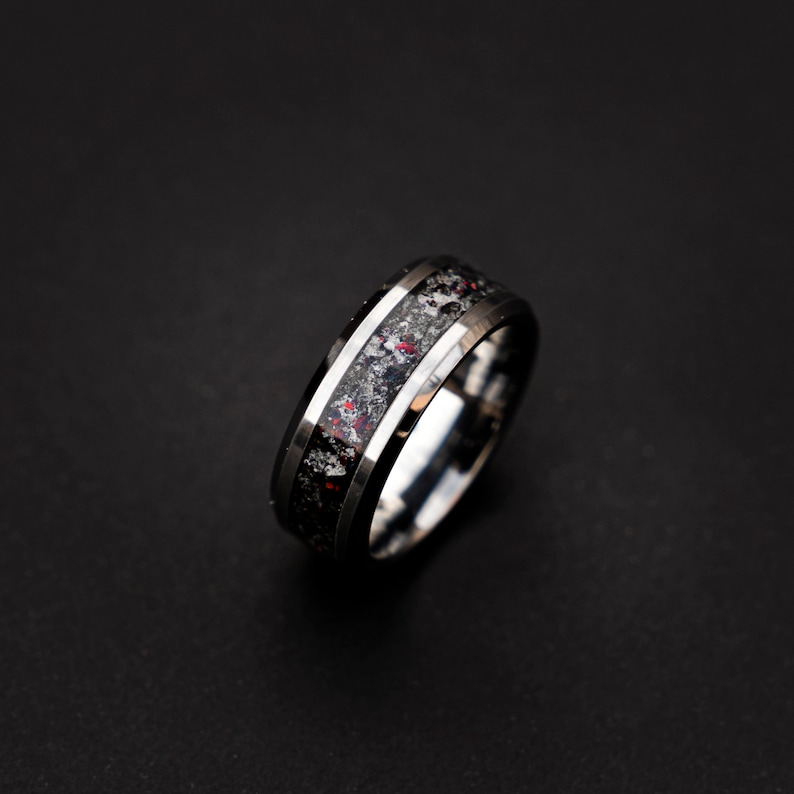 May include: A silver and black tungsten carbide ring with a black and red inlay. The ring has a beveled edge and a polished finish.