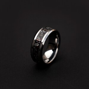May include: A black and silver tungsten carbide ring with a black inlay. The inlay has a speckled pattern of silver and red.