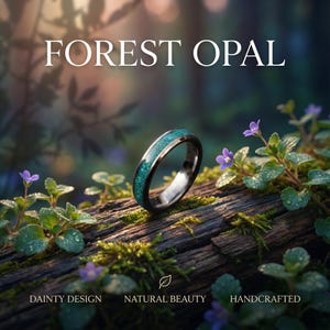 Op de afbeelding: Een ring met een forest opaal ontwerp, met een zwarte band en een levendige turquoise inleg. De ring wordt getoond tegen een natuurlijke achtergrond van mos, hout en kleine paarse bloemen. De tekst op de afbeelding luidt "FOREST OPAL", "DAINTY DESIGN", "NATURAL BEAUTY" en "HANDCRAFTED".
