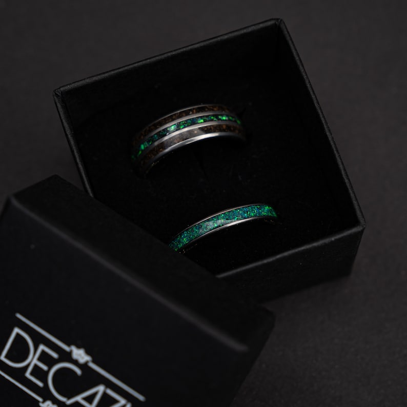 May include: Two black rings with green inlay in a black box. The rings are in a black box with the word "DECAZ" on the front.