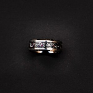 May include: A silver and black ring with a red and white speckled band.
