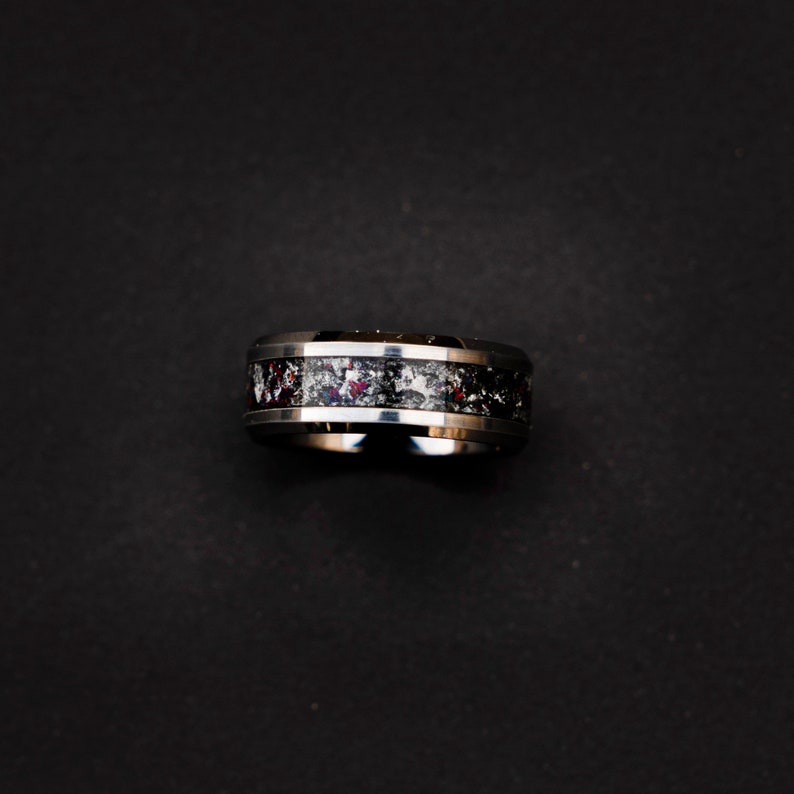 May include: A silver and black ring with a red and white speckled band.