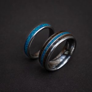 Op de afbeelding: Twee trouwringen, een met een blauwe en zwarte inlay en de andere met een zwarte inlay.