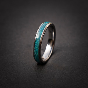 Op de afbeelding: Een zilveren ring met een dunne band en een blauwe opaal-inleg.