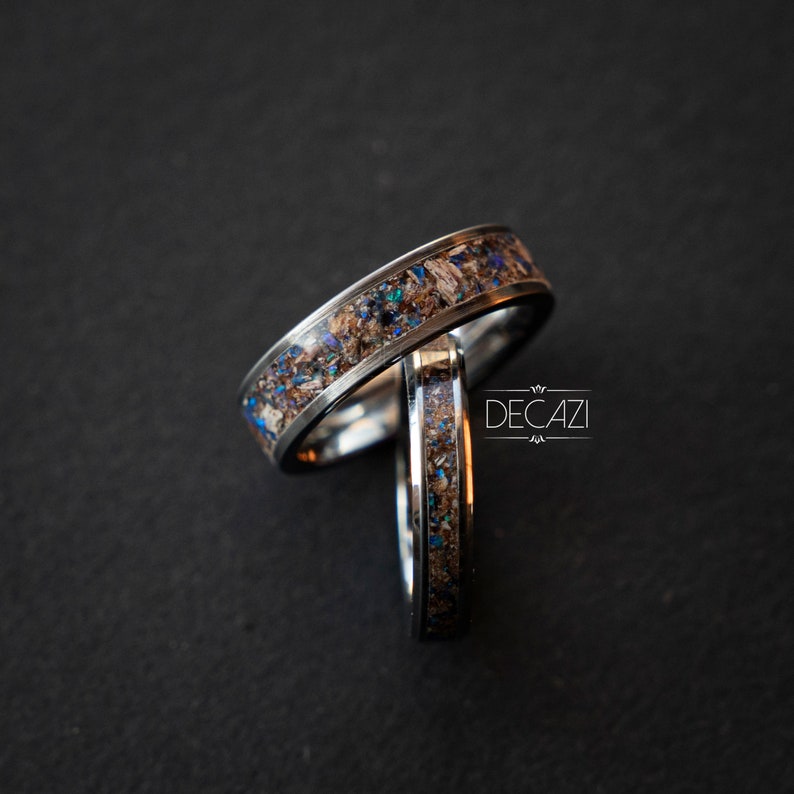 May include: Two silver rings with a unique design featuring embedded blue and brown particles. The rings are stacked on top of each other.