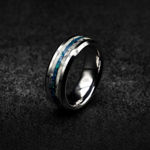 May include: A silver tungsten carbide ring with a blue and white inlay. The ring has a bevelled edge and a polished finish.
