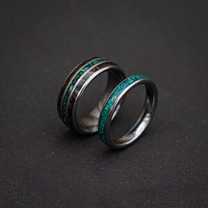 May include: Two silver wedding bands with green opal inlay. The band on the left has a wood inlay.