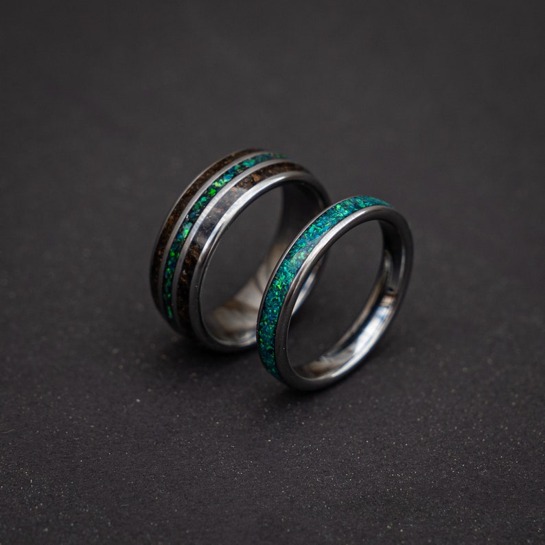 May include: Two silver wedding bands with green opal inlay. The band on the left has a wood inlay.