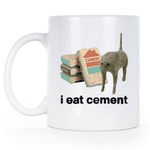 May include: White ceramic mug with a cat illustration and the text "i eat cement". The cat is standing on a stack of cement bags.