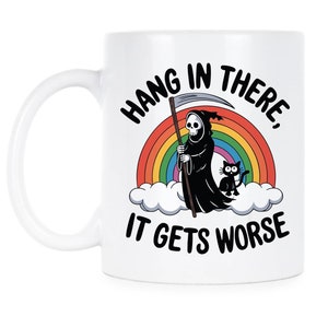 Puede incluir: Taza de café de cerámica blanca con una ilustración en blanco y negro de la Muerte de pie en una nube de arcoíris con un gato negro. El texto en la taza dice "Hang in there, it gets worse".
