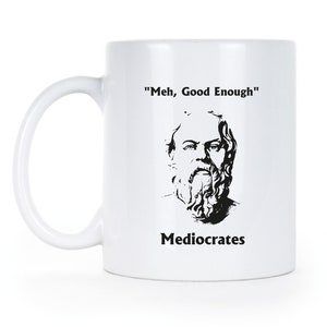 May include: White ceramic mug with a black and white illustration of a man with a beard and the text "'Meh, Good Enough'" and "Mediocrates" printed on it.