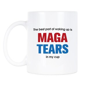 May include: White ceramic coffee mug with the text "The best part of waking up is MAGA TEARS in my cup". The words "Maga" are in red and "Tears" are in blue.