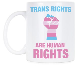 May include: White ceramic mug with a pink and blue transgender pride fist and the text "TRANS RIGHTS ARE HUMAN RIGHTS".