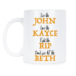 Op de afbeelding: Een witte keramische koffiemok met een zwart en oranje ontwerp. De tekst op de mok luidt "Live like John, Love like Kayce, Fight like Rip, Don't give AF like Beth."