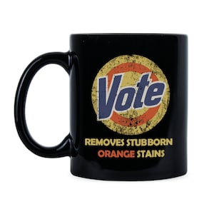 May include: Black coffee mug with a white circle and the word "Vote" in blue letters. The circle has a red and yellow design. The text below the circle reads "Removes Stubborn Orange Stains".