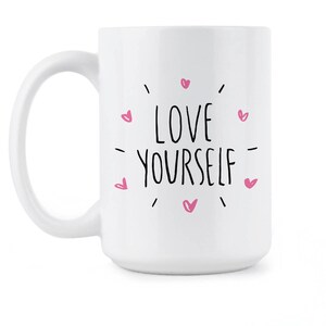 May include: White ceramic coffee mug with a black and pink design. The mug features the text "LOVE YOURSELF" surrounded by pink hearts.