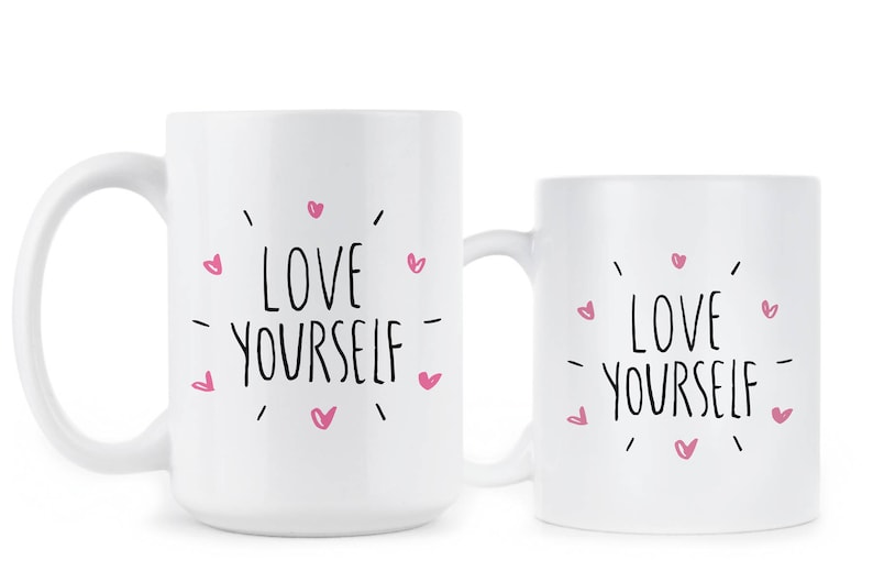 May include: Two white ceramic mugs with black text that reads "LOVE YOURSELF" surrounded by pink hearts.