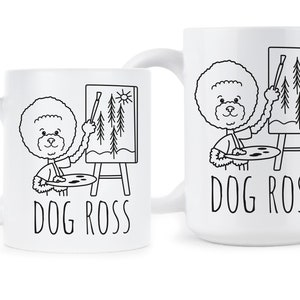 May include: Two white ceramic mugs with black outlines of a dog painting a picture of trees. The text "DOG ROSS" is printed on both mugs.