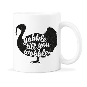 Peut inclure: Une tasse &agrave; caf&eacute; en c&eacute;ramique blanche avec une silhouette noire de dinde et le texte "gobble till you wobble".