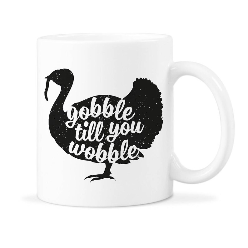 Peut inclure: Une tasse &agrave; caf&eacute; en c&eacute;ramique blanche avec une silhouette noire de dinde et le texte "gobble till you wobble".