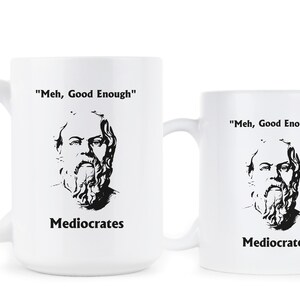 May include: Two white ceramic mugs with black text and a black and white image of a man with a beard. The text on the mugs reads "Meh, Good Enough" and "Mediocrates".