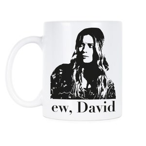 May include: White ceramic coffee mug with a black and white image of a woman with long hair and the text "ew, David".