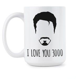 May include: White ceramic coffee mug with a black silhouette of a man's face with a mustache and the text "I love you 3000".