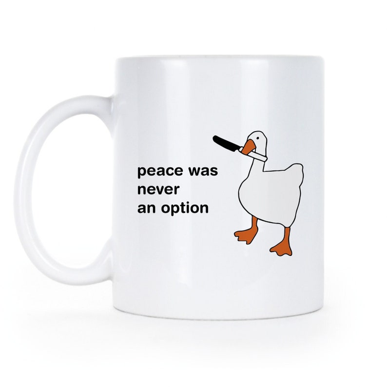 May include: White ceramic mug with a black and white illustration of a goose holding a knife in its beak. The text "peace was never an option" is printed on the mug.