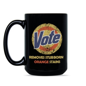 May include: Black coffee mug with a white circle and the word "Vote" in blue text. The circle has a red and yellow design and the text "Removes Stubborn Orange Stains" is below the circle.