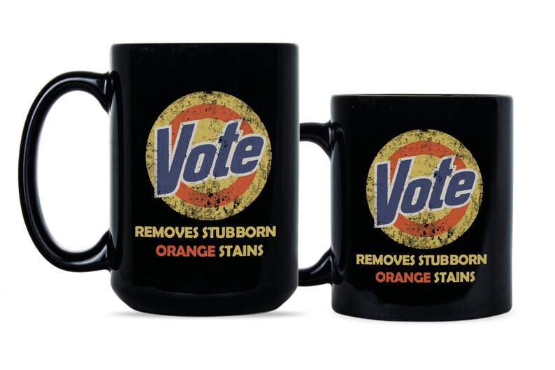May include: Two black coffee mugs with a vintage-style logo that says "Vote" in a blue and yellow circle with an orange ring around it. The text below the logo says "Removes Stubborn Orange Stains".