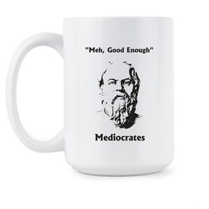 May include: White ceramic mug with a black and white illustration of a man with a beard and the text "'Meh, Good Enough'" and "Mediocrates" printed on it.