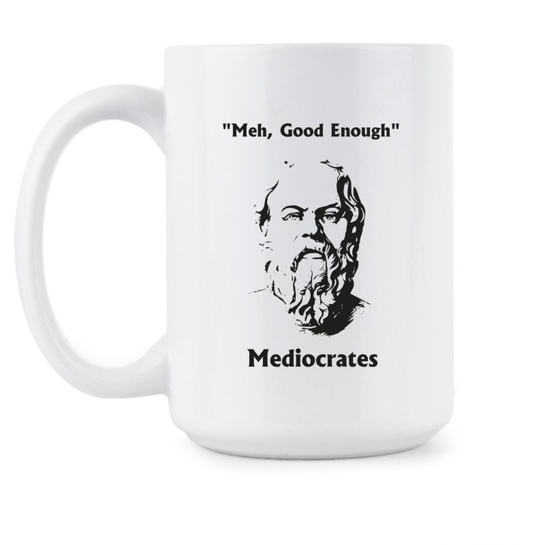 May include: White ceramic mug with a black and white illustration of a man with a beard and the text "'Meh, Good Enough'" and "Mediocrates" printed on it.
