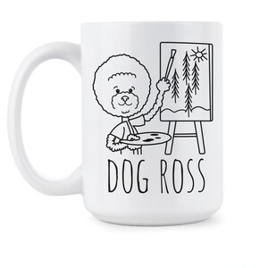 May include: White ceramic coffee mug with a black and white illustration of a dog painting a landscape on a canvas. The text "DOG ROSS" is printed below the illustration.