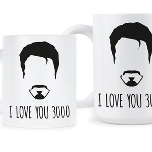 May include: Two white ceramic mugs with black silhouettes of a man's face and the text "I love you 3000".