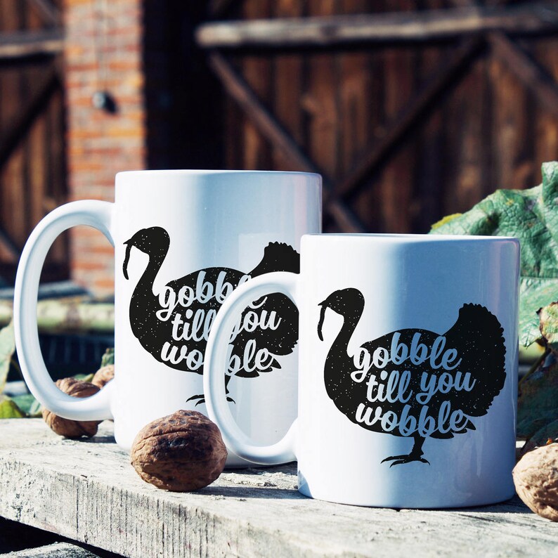 Peut inclure: Deux tasses en c&eacute;ramique blanche avec des silhouettes de dindes noires et le texte "gobble till you wobble".