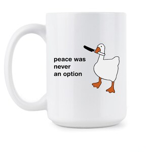 May include: White ceramic mug with a black and white illustration of a goose holding a knife in its beak. The text "peace was never an option" is printed on the mug.