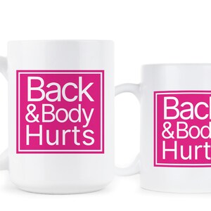 May include: Two white coffee mugs with a pink square design that says "Back & Body Hurts" in white text.