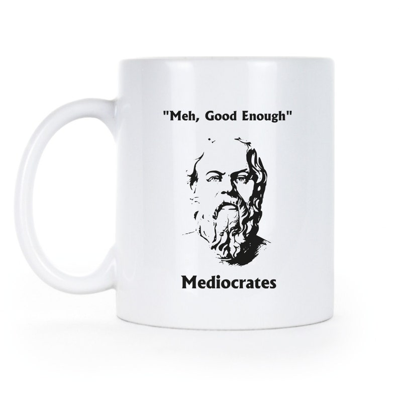 May include: White ceramic mug with a black and white illustration of a man with a beard and the text "'Meh, Good Enough'" and "Mediocrates" printed on it.